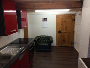 A kitchen with red cabinets, a black countertop, a wooden door, and a green armchair. - 325 Year Old Swiss Chalet (Boltigen)