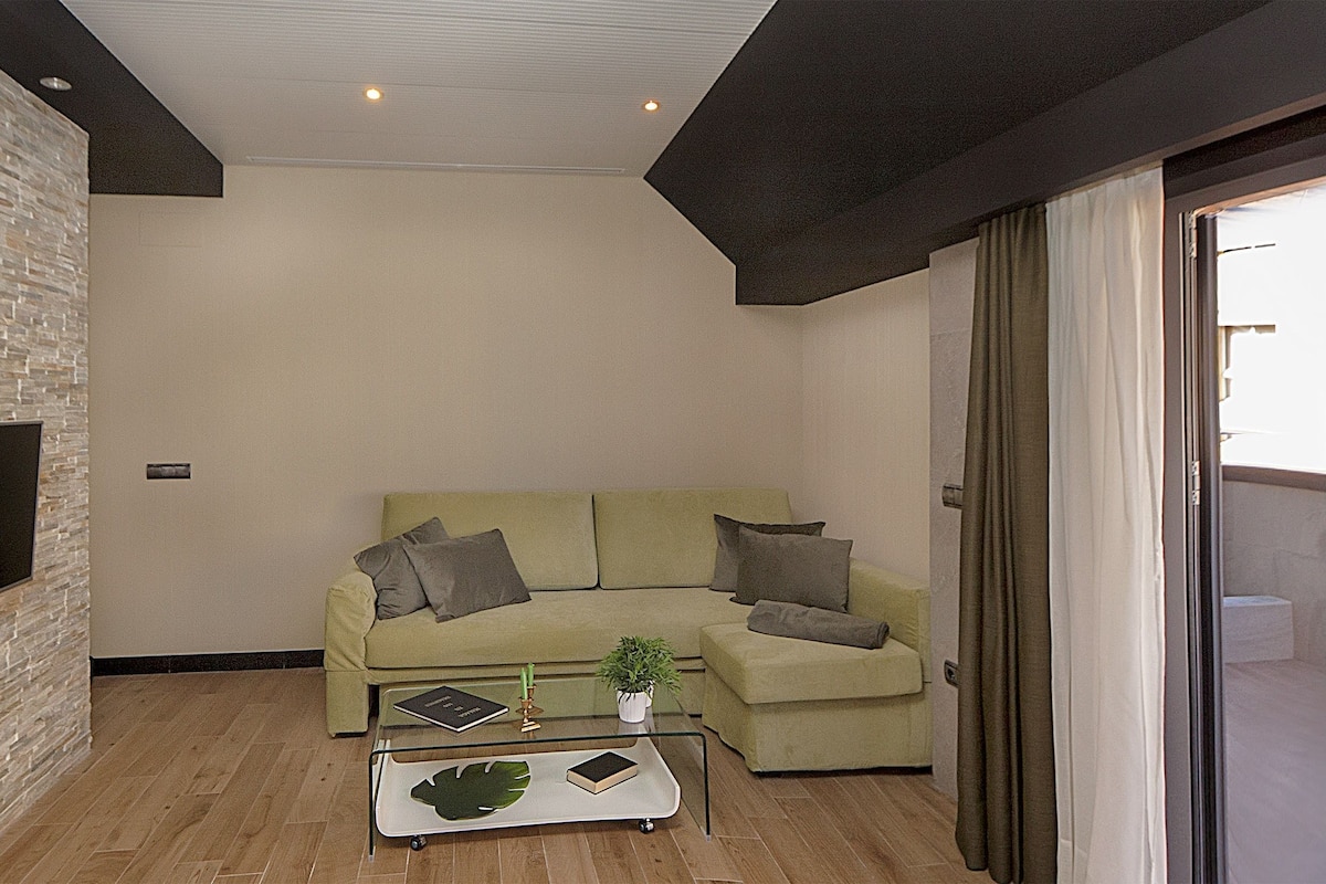 Ein modernes Wohnzimmer mit Steinwand, Flachbildfernseher, grünem Sofa mit Kissen, Glastisch mit Dekoration und einer Schiebeglastür.
