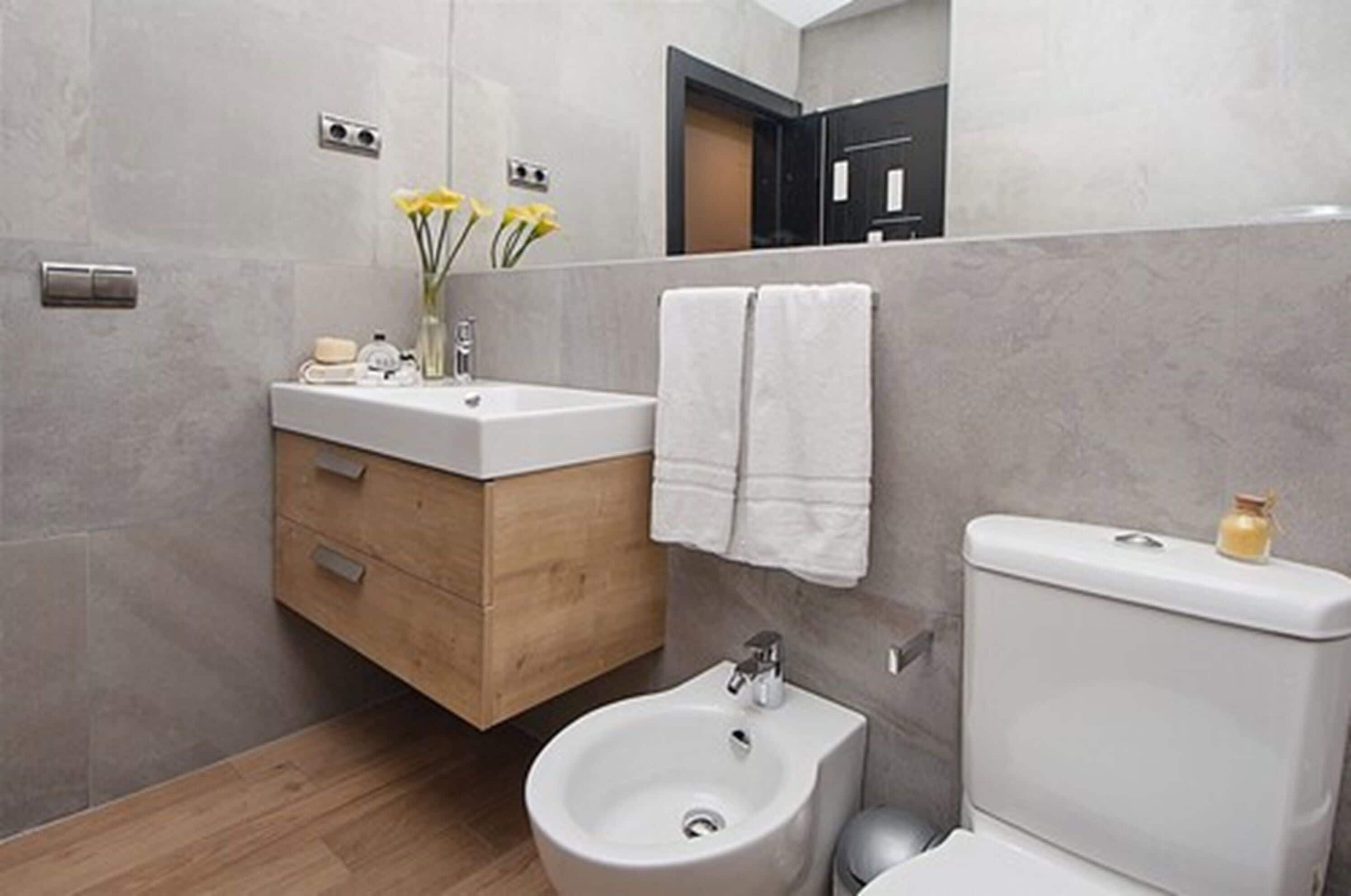 A modern bathroom with a wooden vanity, a bidet, and a toilet.