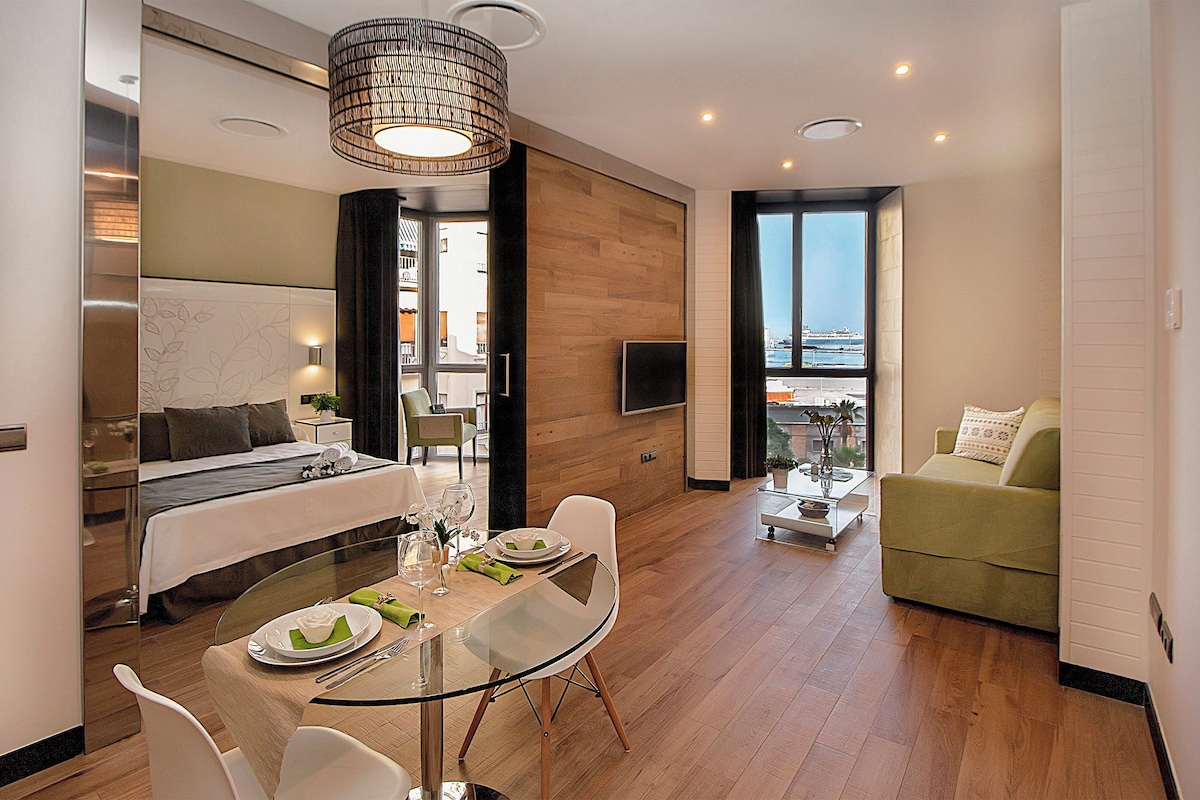 A modern hotel room with a glass dining table, a sofa, a bed, and a balcony with a view.