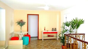 A living room with a white sofa, a red ottoman, a glass coffee table, and a potted plant. - Hostel da Barra (Rio de Janeiro)