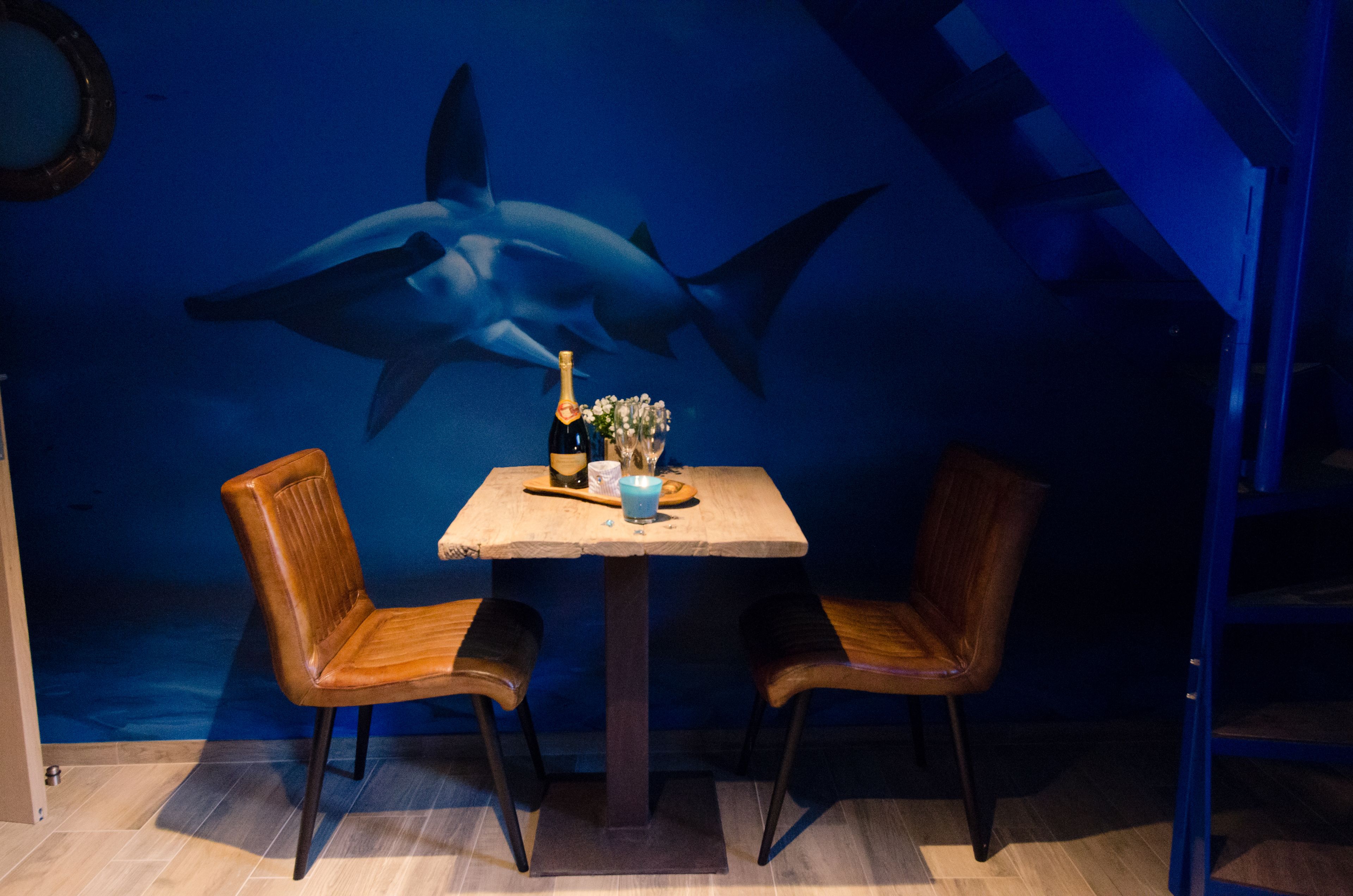A dining area with a table set for two, featuring a bottle of champagne and a vase of flowers.