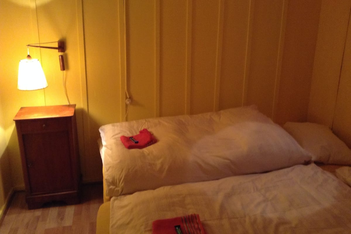 A room with two beds, a nightstand with a lamp, and a wall-mounted telephone.