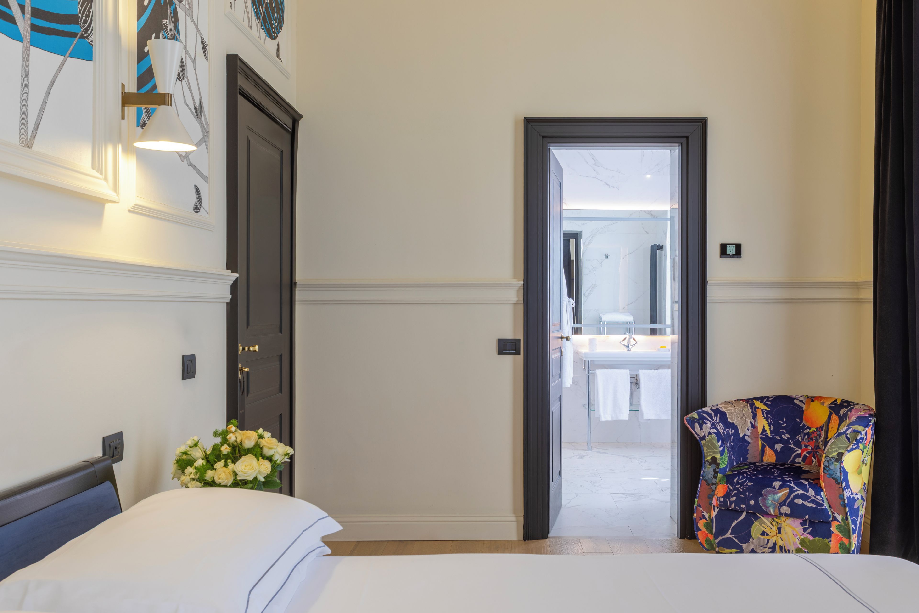 Una camera d'albergo con un letto, una sedia, un ingresso che porta al bagno e una parete con l'orologio.