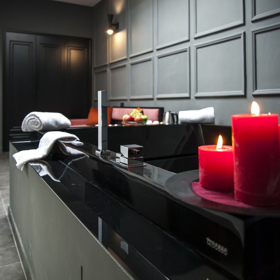 A modern bathroom with a black countertop, a towel, and two red candles.