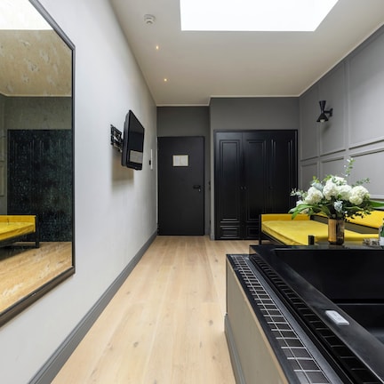 A modern bathroom with a large mirror, a black bathtub, yellow vanity, and a door leading to another room.