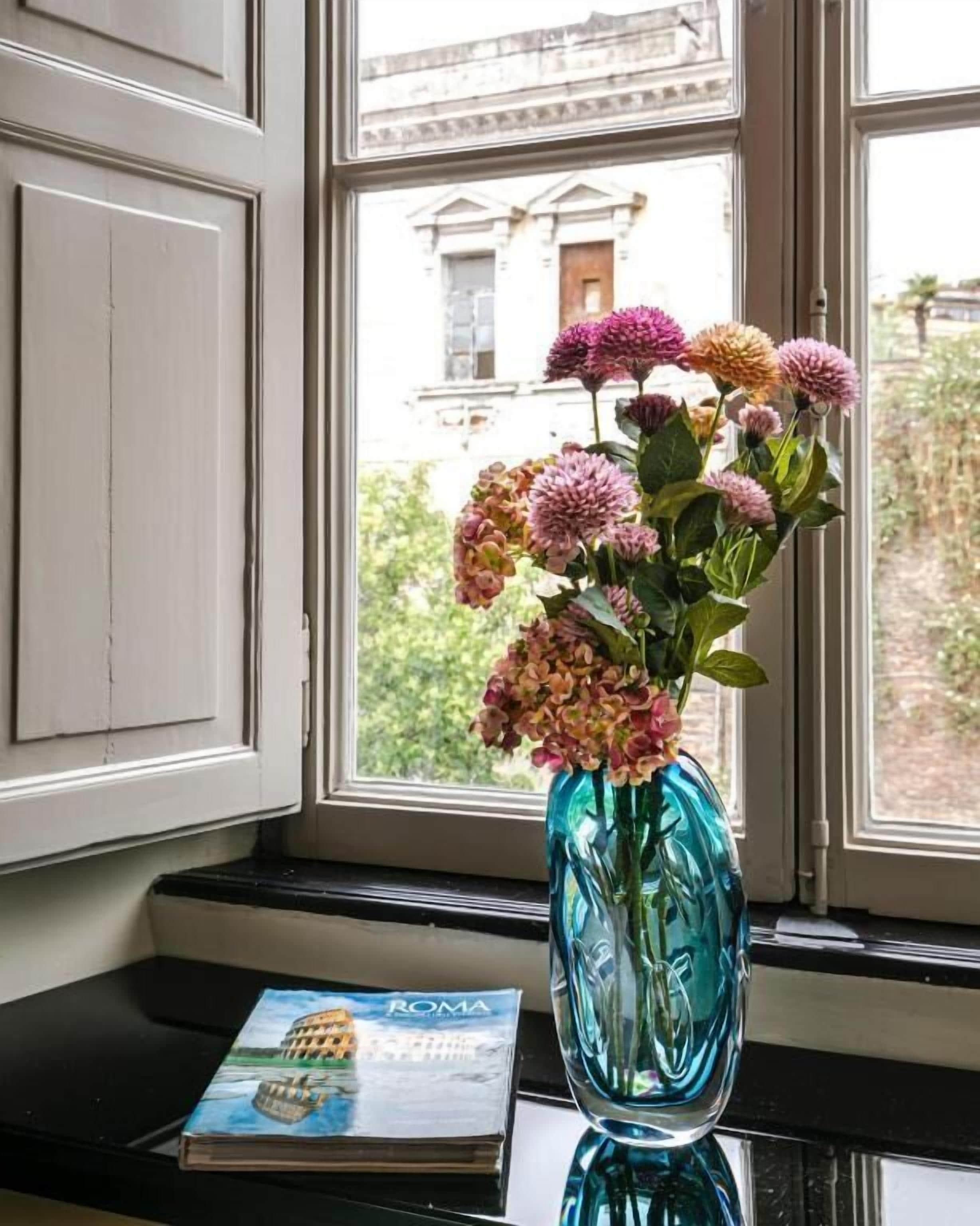 A window with a vase of flowers on a windowsill and a book titled "ROMA" beside it.