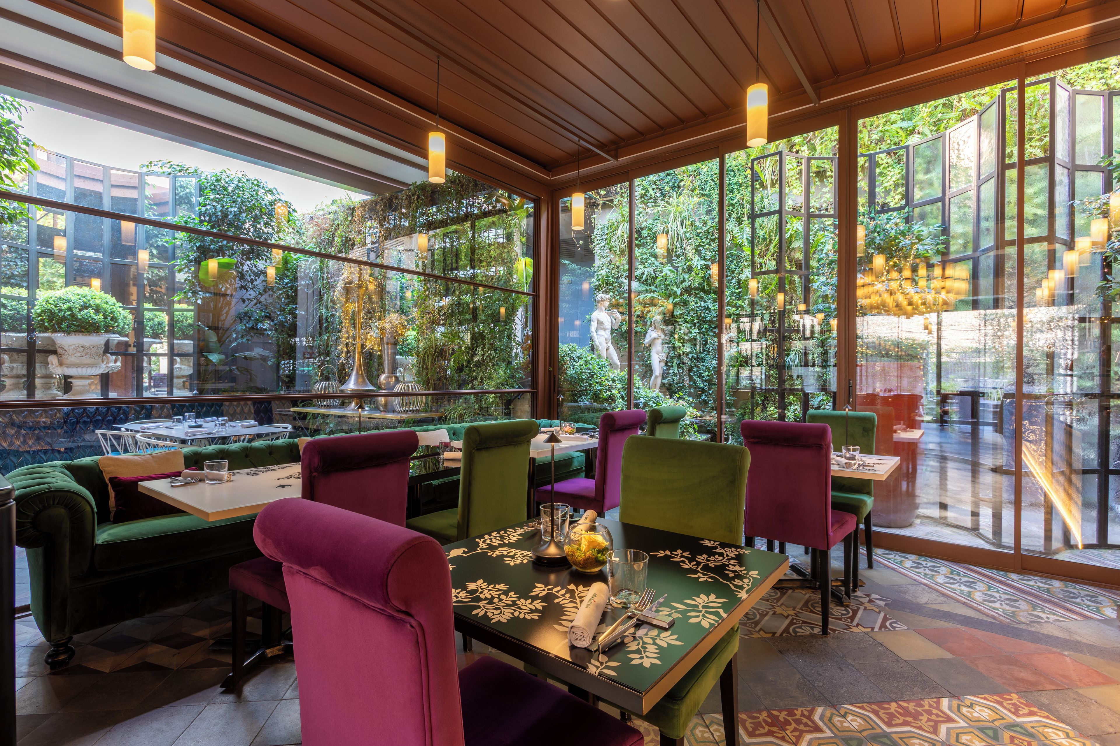 Un restaurante con vistas a un follaje exuberante a través de amplios ventanales, vigas de techo de madera y sillas tapizadas de colores.