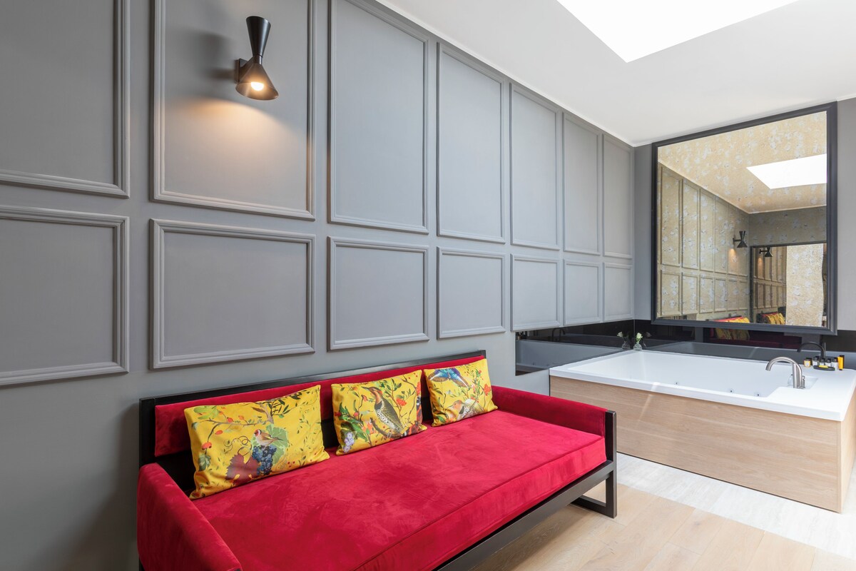 A modern bathroom with a large mirror, a white sink, and a red sofa with floral cushions.