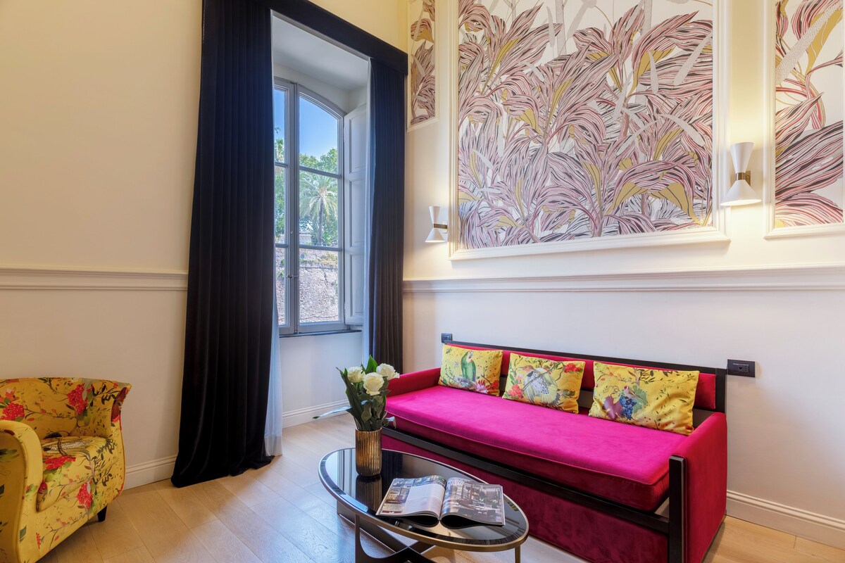 A room with a red sofa, a yellow armchair, a glass coffee table, and a large window with curtains.