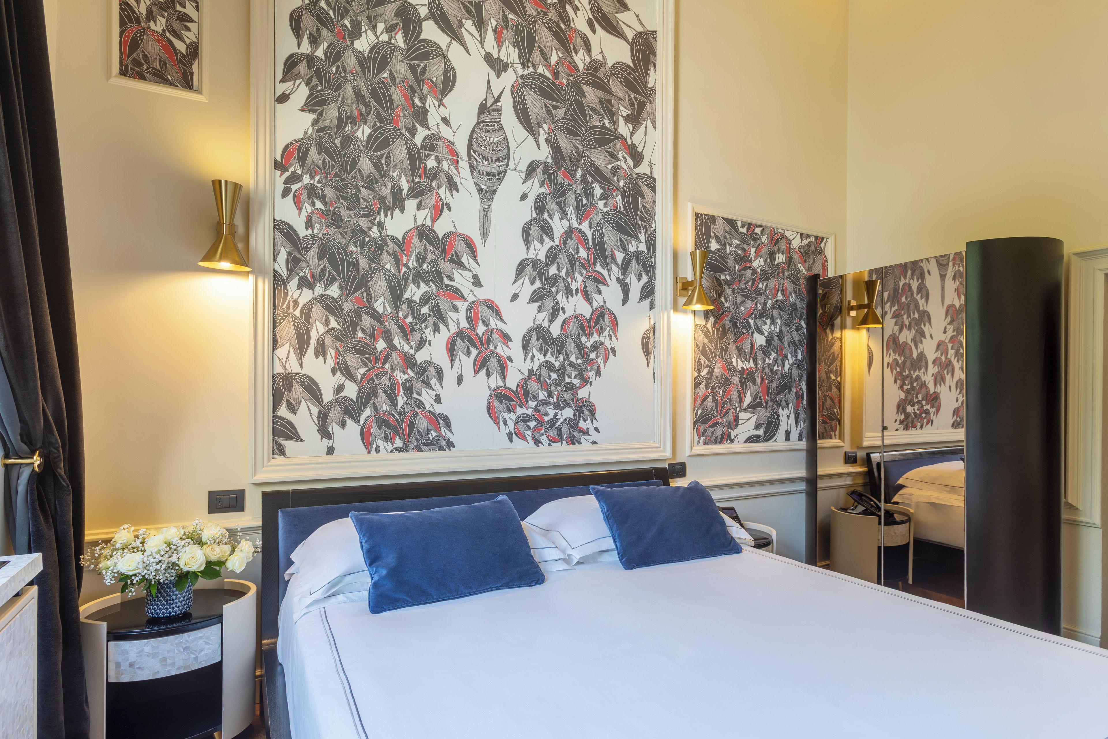 A hotel room with a large bed, two bedside lamps, a nightstand with a vase of flowers, and a mirror on the wall.