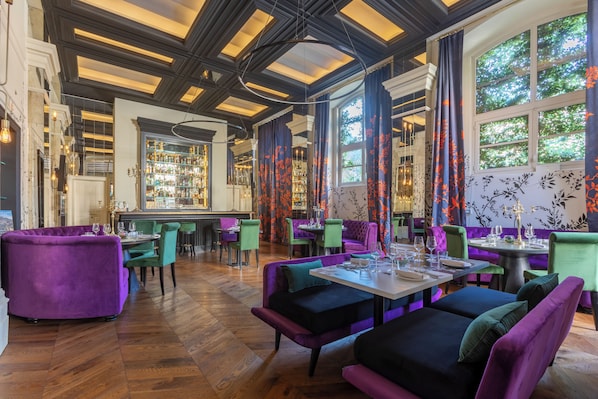 A restaurant interior with wooden flooring, purple and green upholstered seating, and a bar area with glassware.