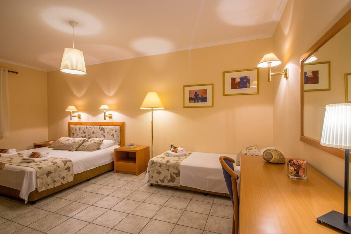 A hotel room with two beds, a desk, a chair, a lamp, a nightstand, and framed pictures on the wall.