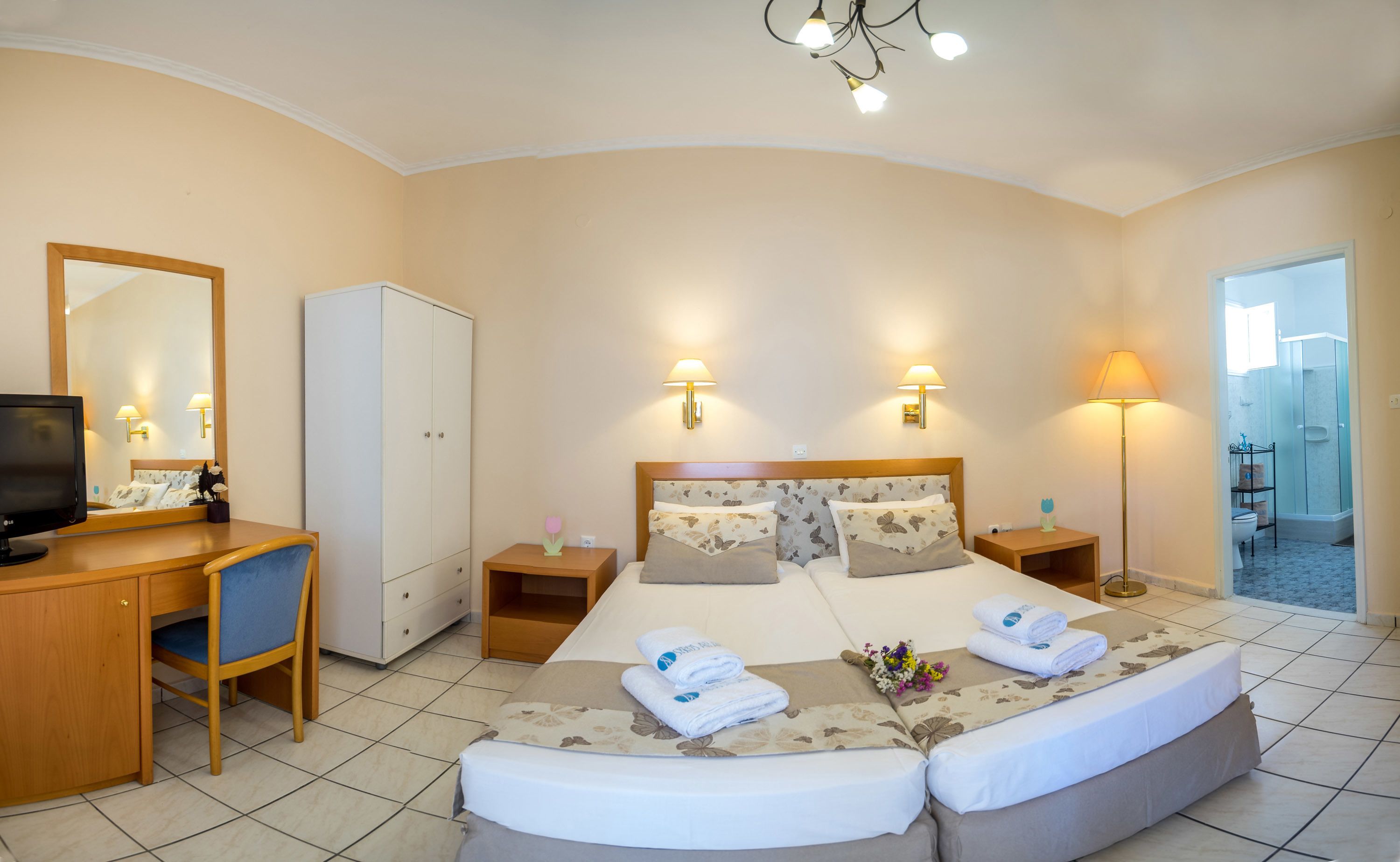 A hotel room with a bed, a desk, a television, a wardrobe, and a bathroom visible through an open door.
