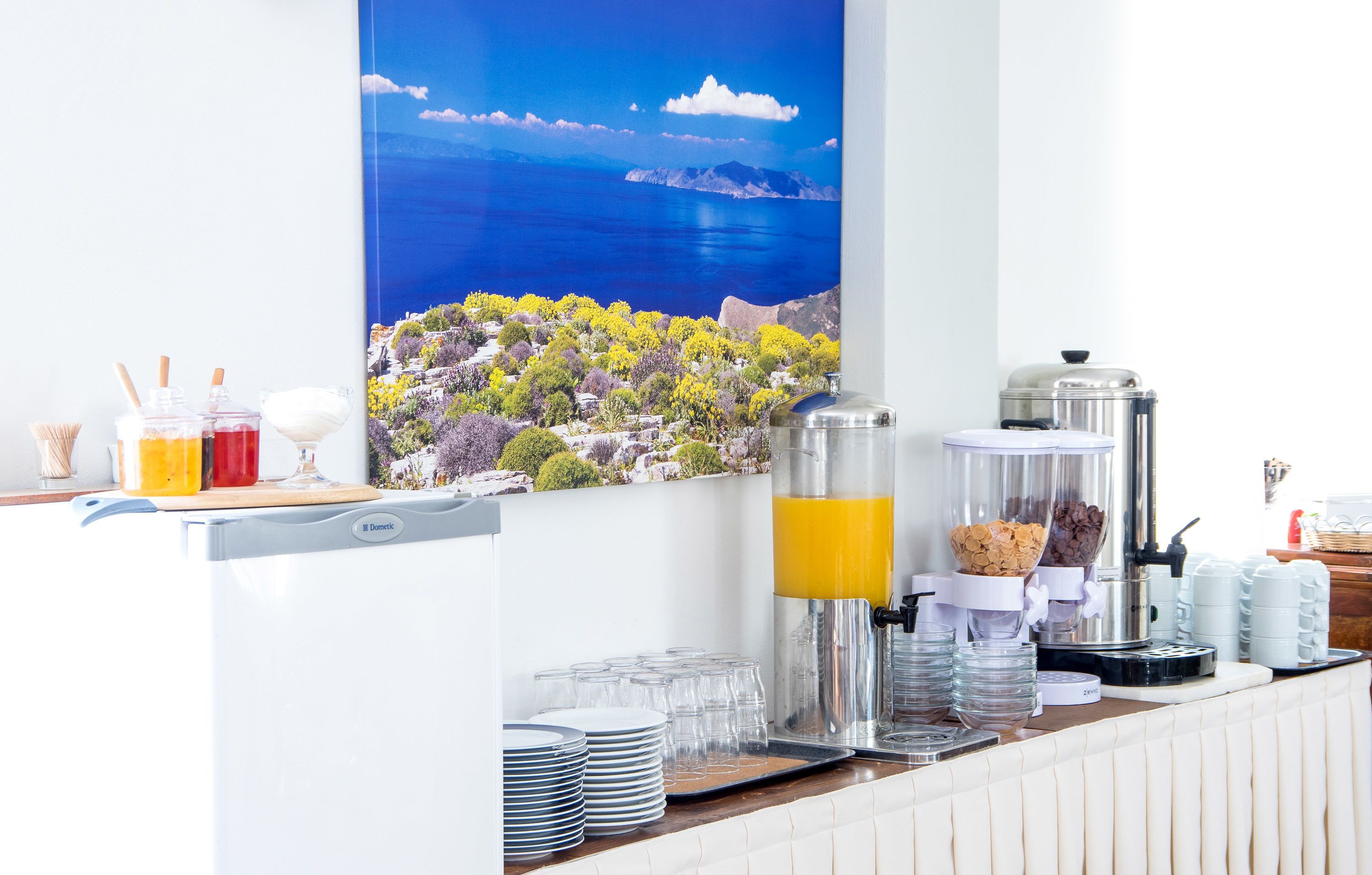 Un bar où l’on peut prendre le petit-déjeuner, offrant une vue sur un paysage côtier, avec la mer et des montagnes en arrière-plan.