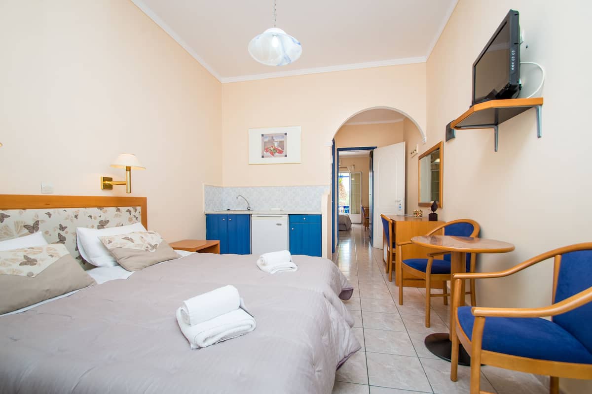 A hotel room with a bed, a desk, a chair, a TV, and a kitchenette.