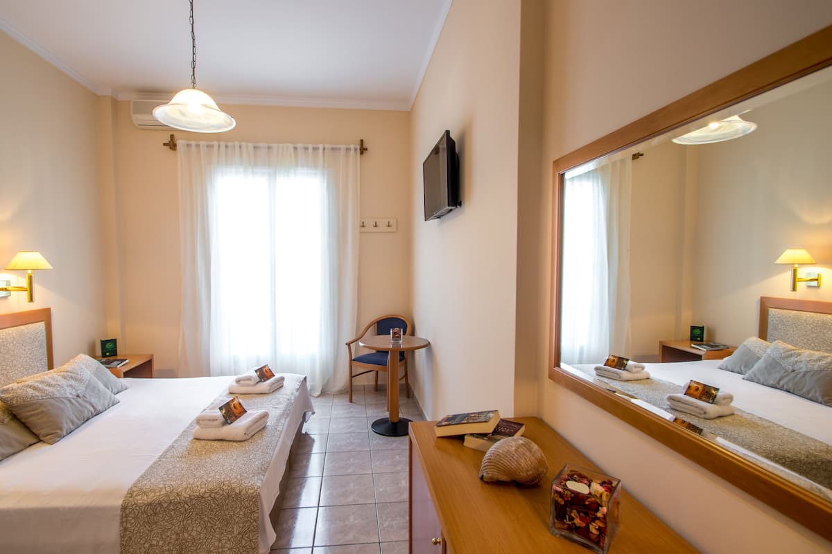 A hotel room with two beds, a desk, a chair, a TV, and a large mirror.