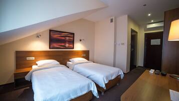 A hotel room with two beds, a wooden headboard, a painting, a desk with a lamp, and a door with a sign.