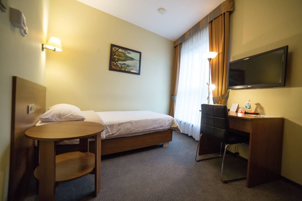 Een hotelkamer met een bed, bureau, stoel, klein tafeltje, televisie en een schilderij aan de muur.