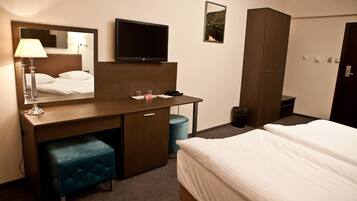 A hotel room with a bed, a desk with a chair, a mirror, a television, and a wardrobe.