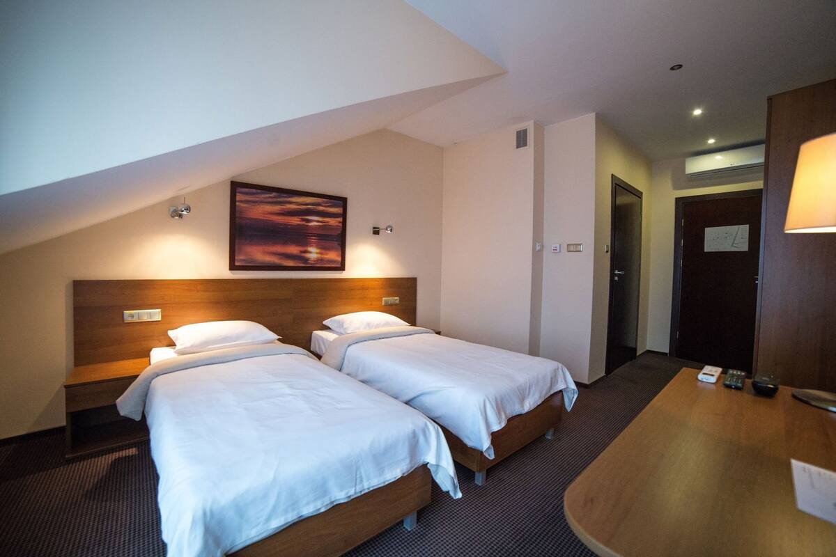 Een hotelkamer met twee bedden, een houten hoofdbord, een schilderij, een bureau met een lamp en een deur.