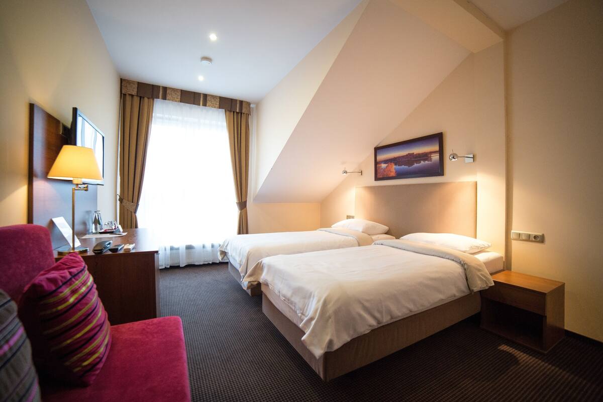 Een hotelkamer met twee bedden, een bureau, een stoel en een schilderij aan de muur.