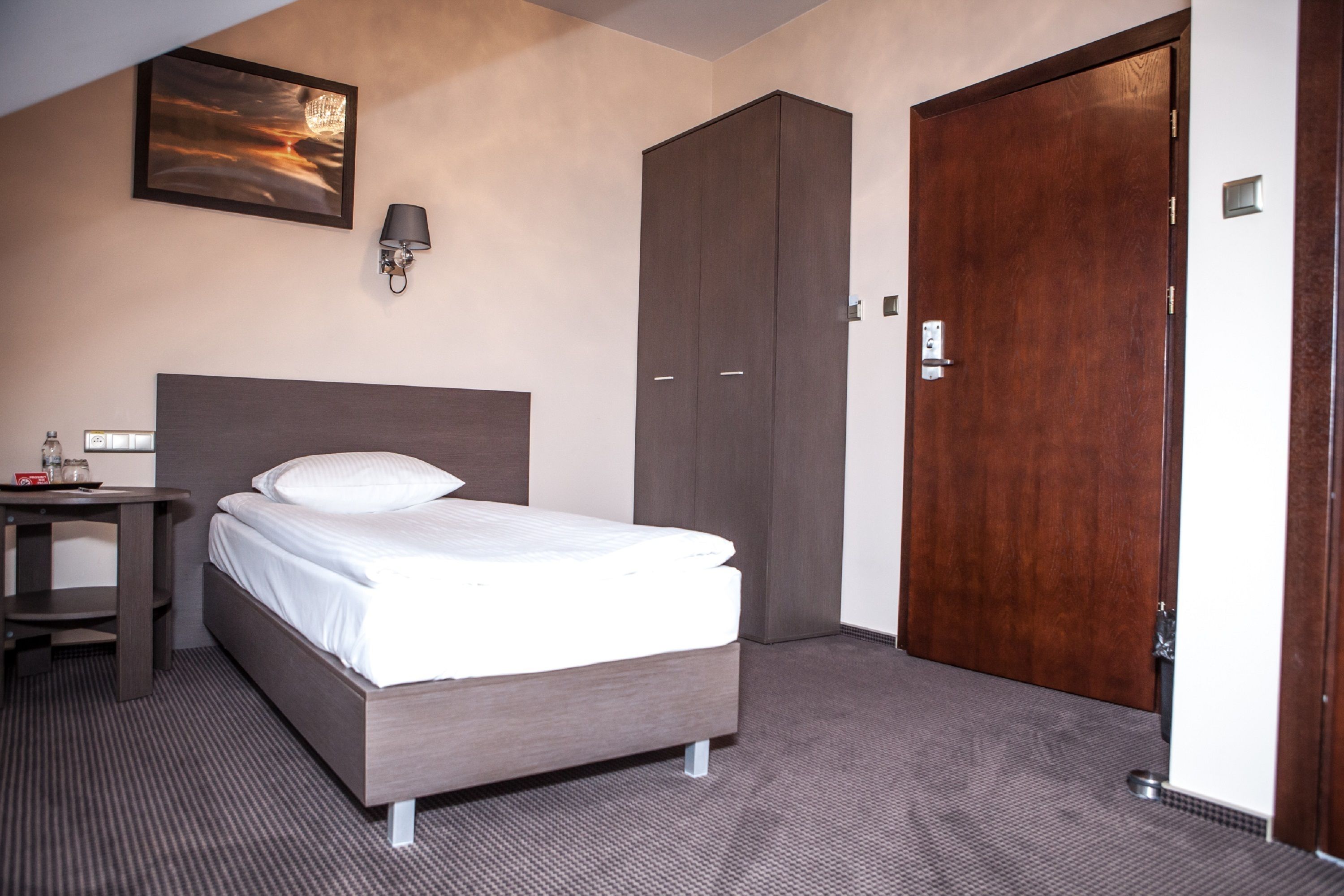 A hotel room with a bed, a nightstand, a wardrobe, and a door.