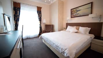 A hotel room with a large bed, a desk, a chair, a lamp, and a painting on the wall.