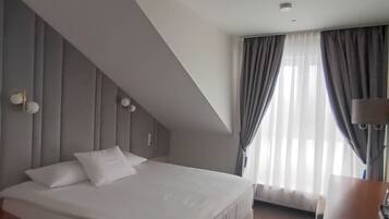 A modern hotel room with a large bed, a desk, and a window with curtains.