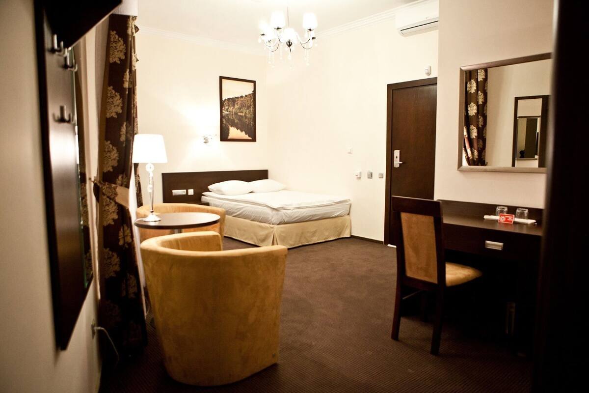 Hotelkamer met een bed, bureau, stoel, lamp, kroonluchter, spiegel en een schilderij aan de muur.