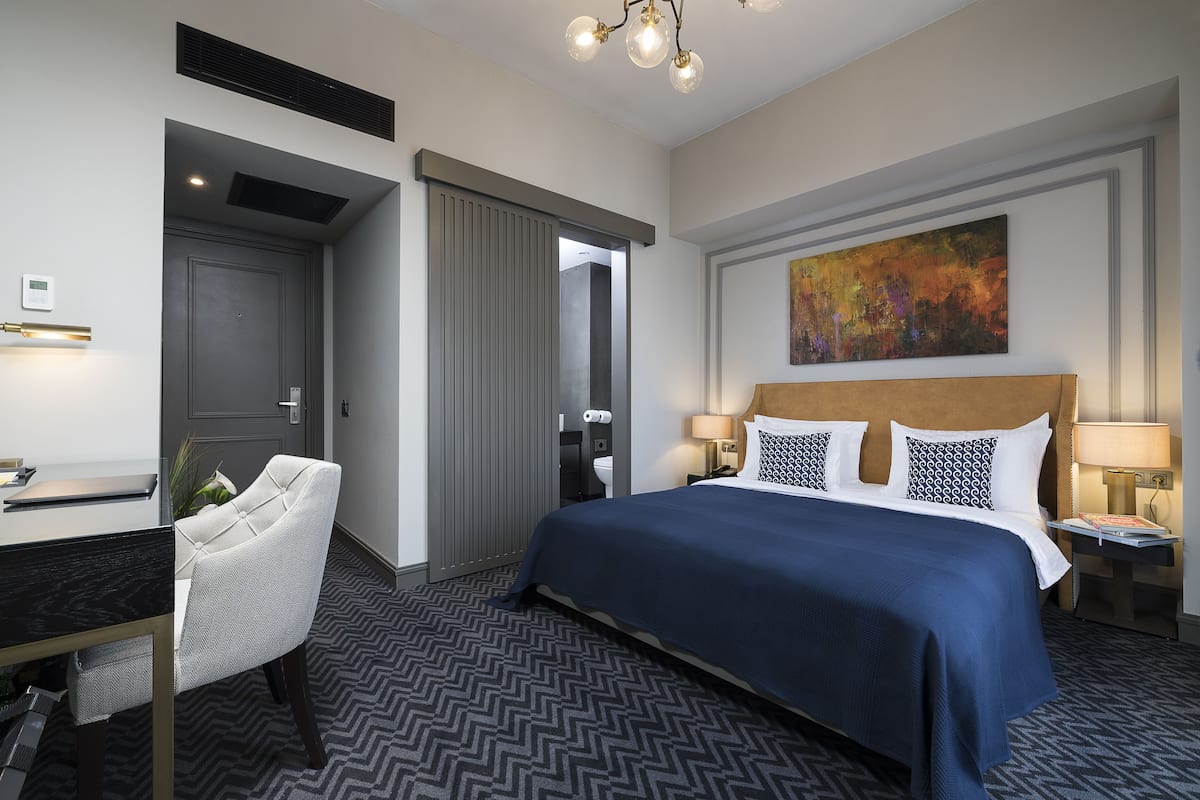 Una habitación de hotel con cama, escritorio, silla, un cuadro y alfombra estampada.