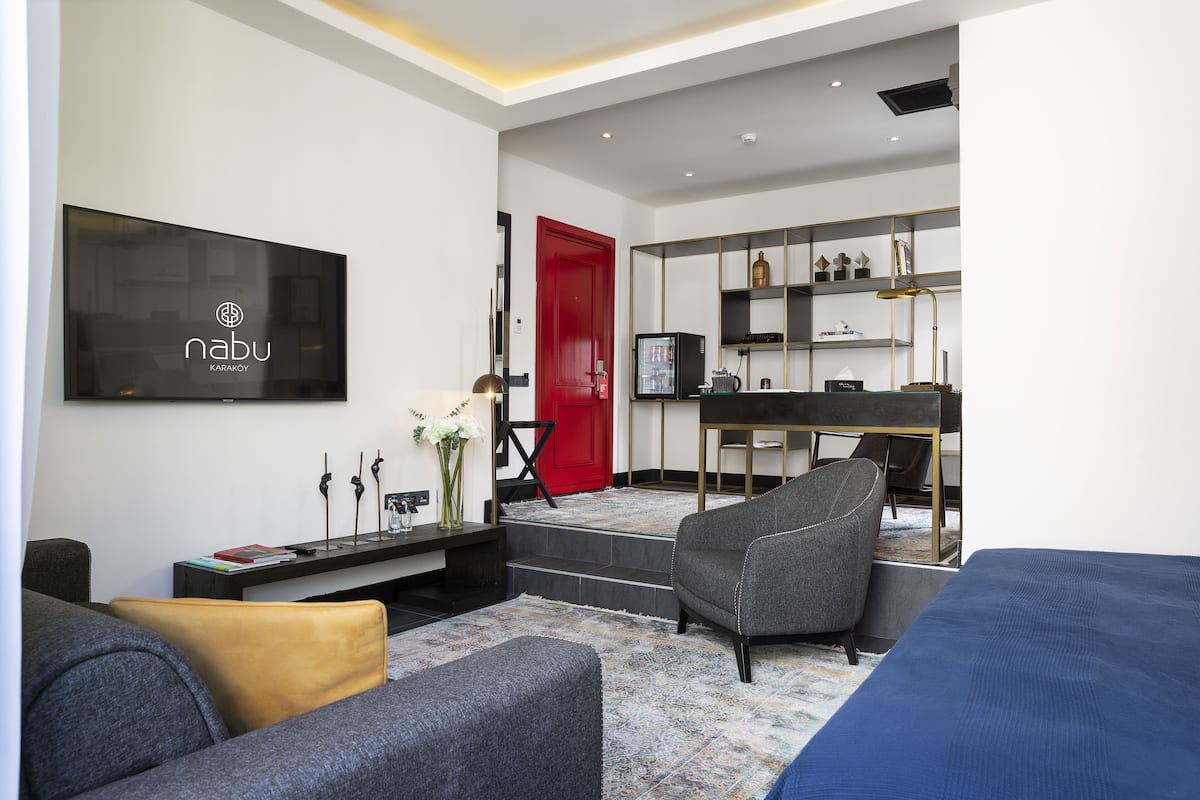 Una sala de estar moderna con televisor, sofá y una zona de escritorio con computadora y estanterías.