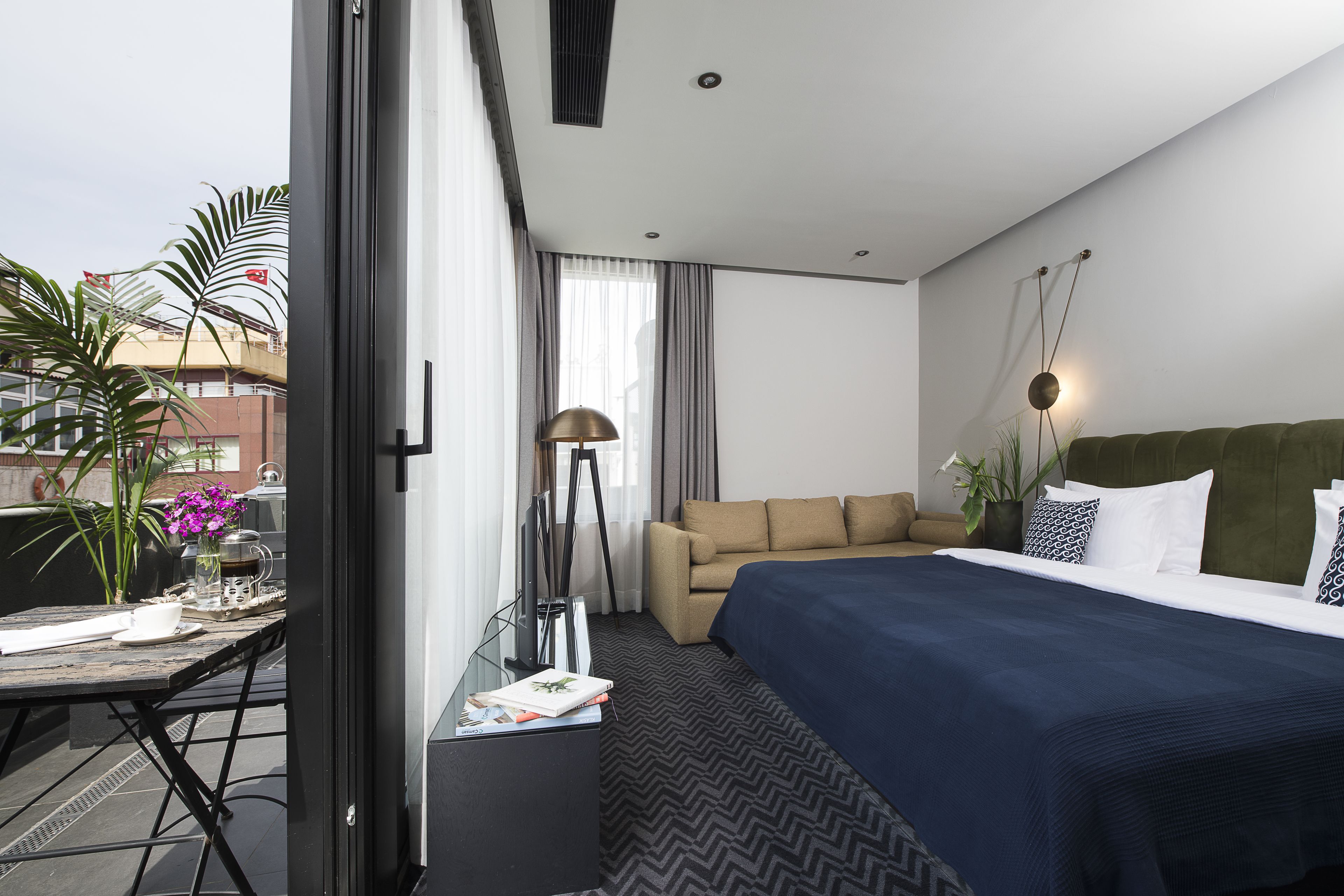 A hotel room with a bed, a sofa, a dining table with a vase of flowers, and a view of the outside.