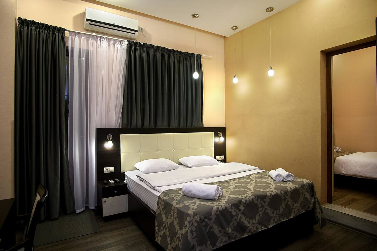 Ein Hotelzimmer mit Bett, Nachttisch, Spiegel und einem Fenster mit Vorhängen.