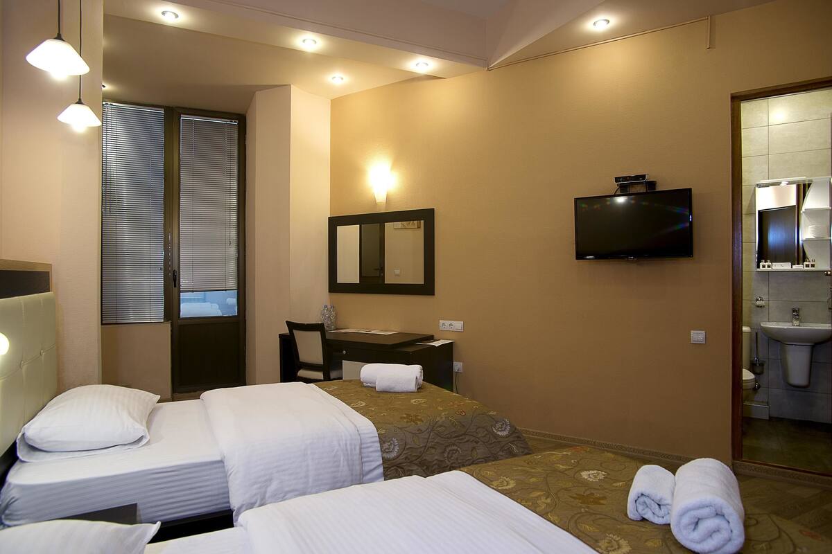 Ein Hotelzimmer mit zwei Betten, einem Schreibtisch, einem Fernseher und einem durch eine offene Tür einsehbaren Badezimmer.