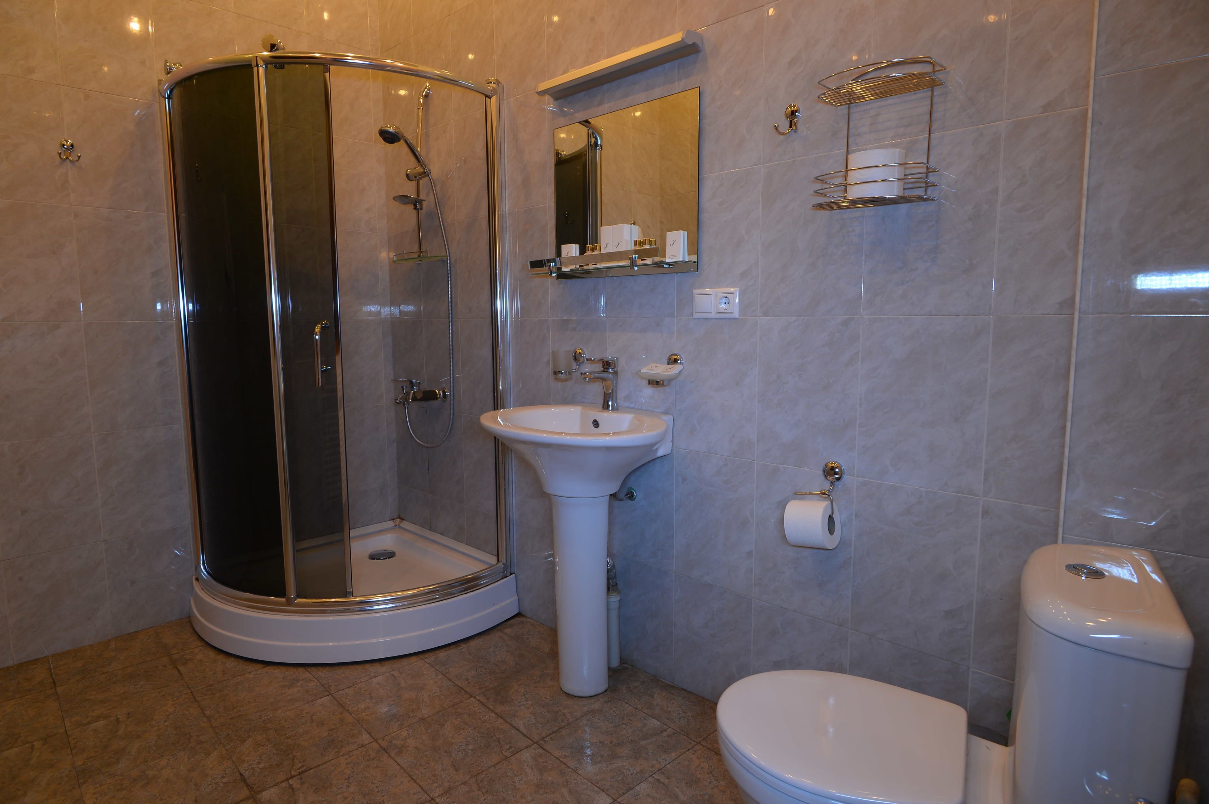 Ein Badezimmer mit einer Duschkabine, einem Standwaschbecken, einer Toilette und einem Spiegel über dem Waschbecken.