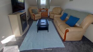 Een woonkamer met een bank, stoelen, een salontafel, een televisie en een raam met gordijnen.
