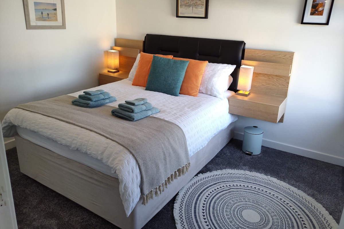 A neatly made bed with a headboard, two bedside lamps, and a small waste bin.
