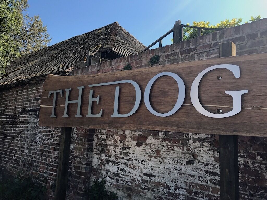 Un senyal de fusta amb el text "THE DOG" muntat sobre un mur de rajola.