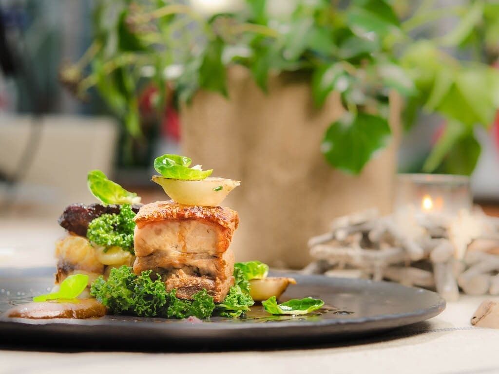 A plate of food with a variety of vegetables and a piece of meat, possibly pork, on a dark plate.