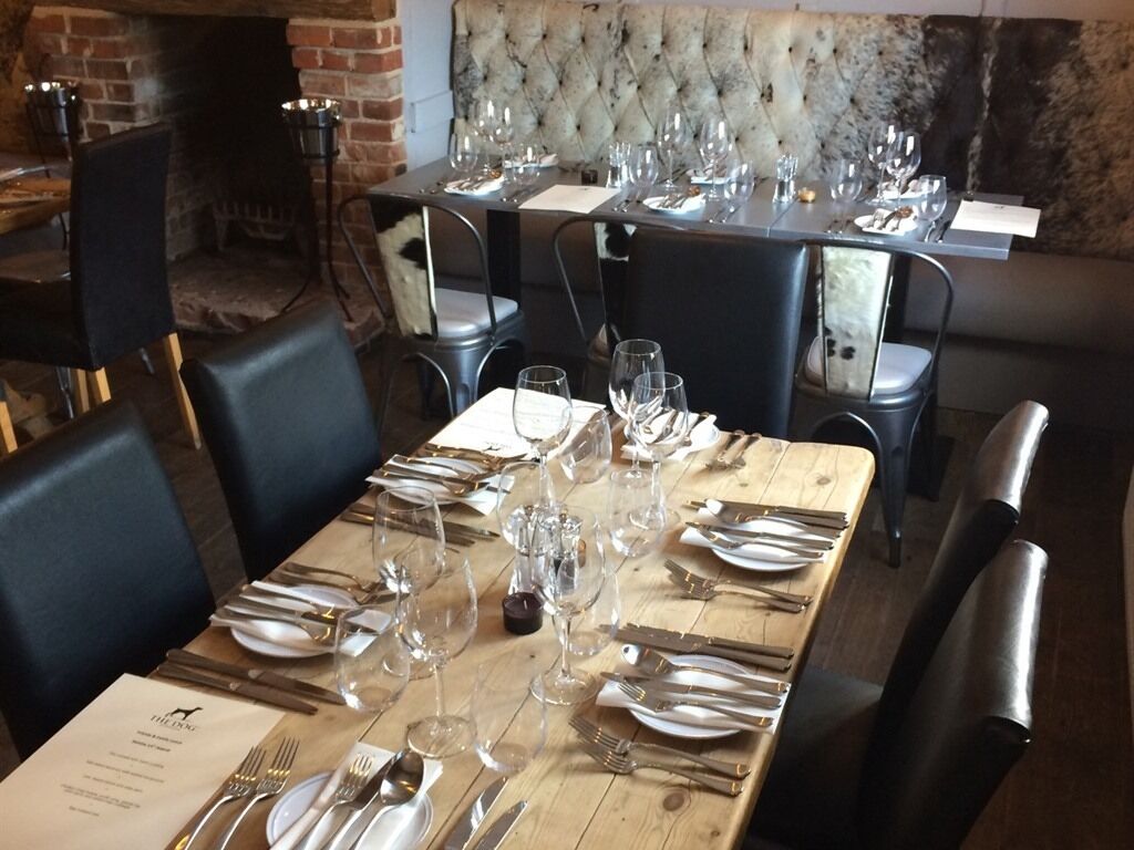 Un restaurant doté de nombreuses tables dressées pour le service, avec une cheminée en briques et une tête de lit capitonnée en arrière-plan.