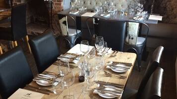 Un restaurant doté de nombreuses tables dressées pour le service, avec une cheminée en briques et une tête de lit capitonnée en arrière-plan.