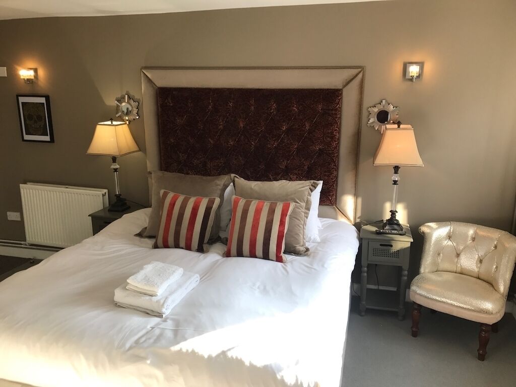 A neatly made bed with pillows, a headboard, two bedside lamps, a radiator, and a chair.