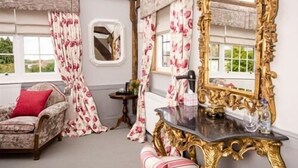 A room with a large ornate mirror, floral curtains, a patterned sofa, and a small table with a vase. - The Dog at Wingham (Canterbury)