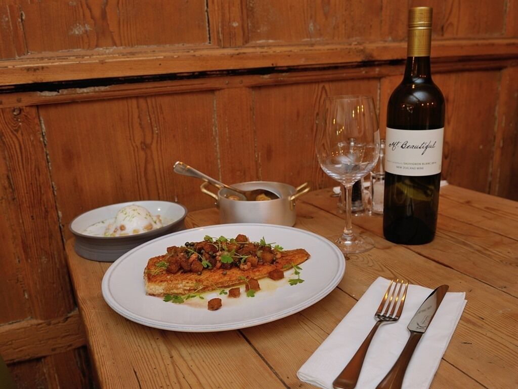 A wooden table with a plate of food, a bottle of wine, and a glass.