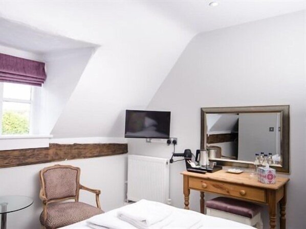 A hotel room with a bed, a wooden dresser, a chair, a television, and a window with a view of greenery. - The Dog at Wingham (Canterbury)