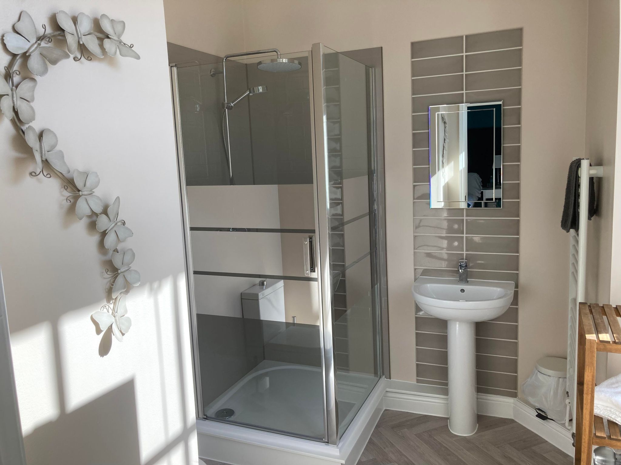 A modern bathroom with a glass-enclosed shower, a white pedestal sink, and a mirror above the sink.