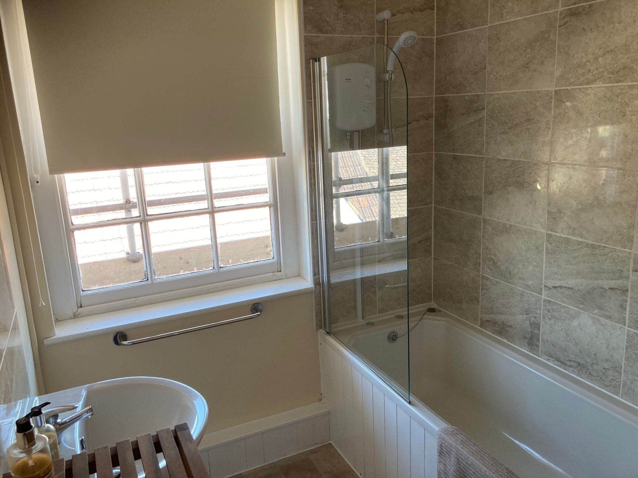 A bathroom with a bathtub, a glass-enclosed shower, a window, and a sink with soap dispensers.