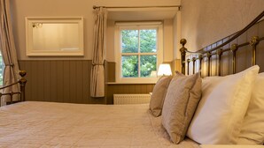 A bedroom with a large bed, a window with curtains, a radiator, and a bedside table with a lamp. - The Swan Hotel (Wotton-under-Edge)