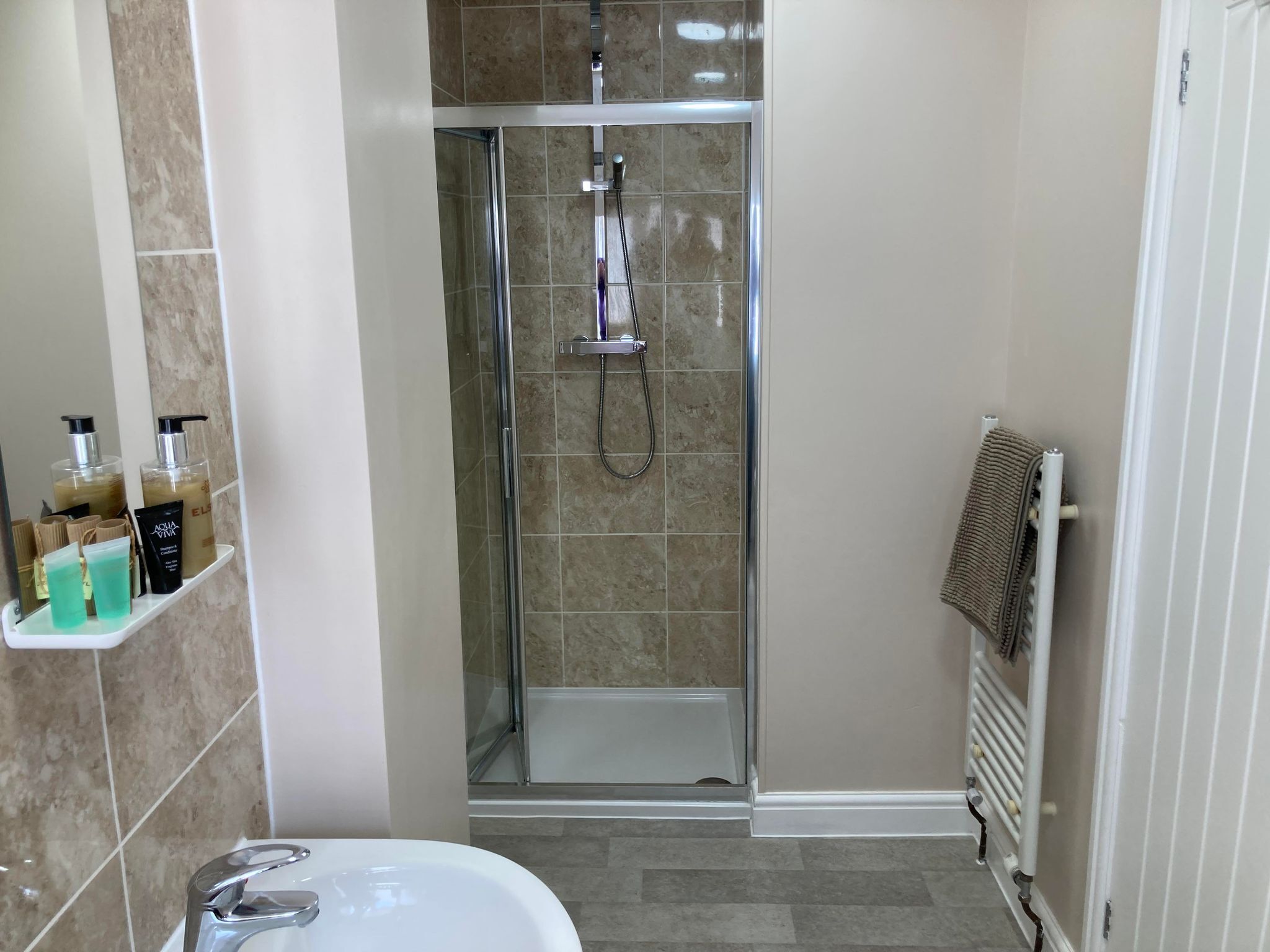 A modern bathroom with a glass-enclosed shower, a white sink, and a towel rack.